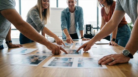 Young diverse team pointing at documents on wooden table during brainstorming meeting in bright modern office space
